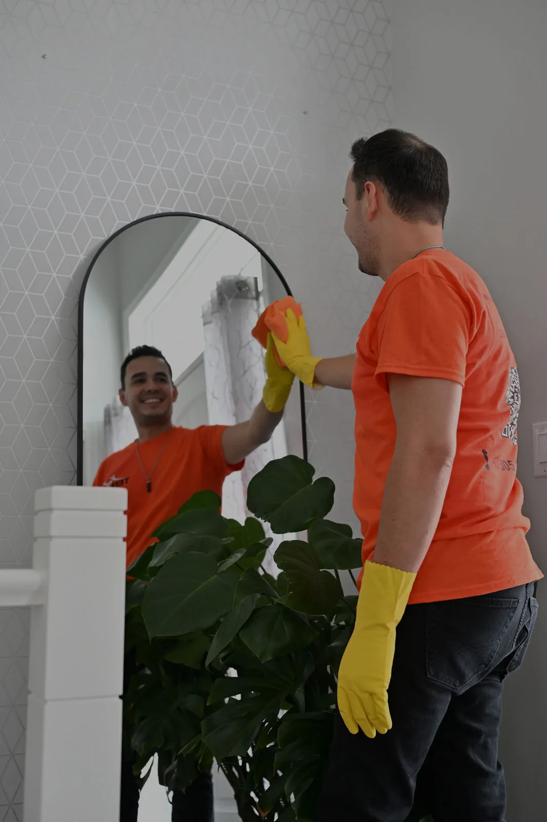 Man cleaning mirror in front of plant